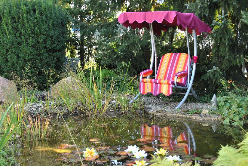Dondolo monoposto Angerer con cuscini a righe accanto a un laghetto in giardino